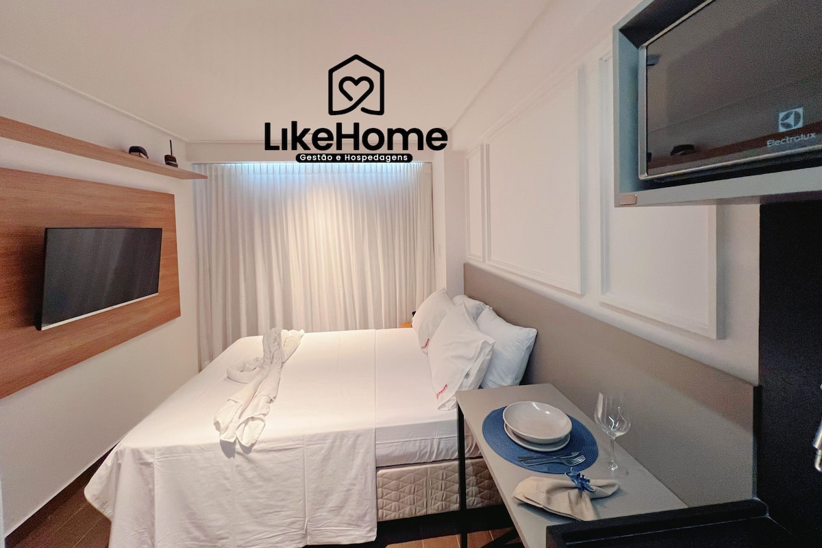 A hotel room with a bed, a TV, a table with a plate and glass, and a window with curtains.