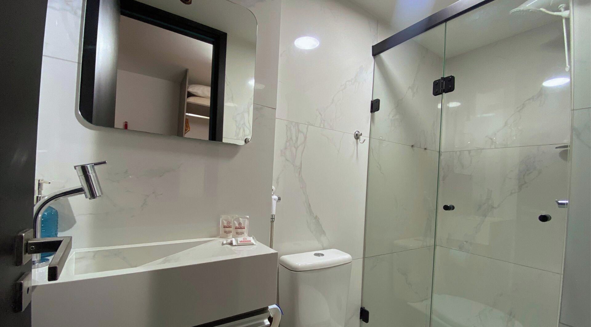 A modern bathroom with a glass-enclosed shower, a white sink with a mirror above it, and a toilet.