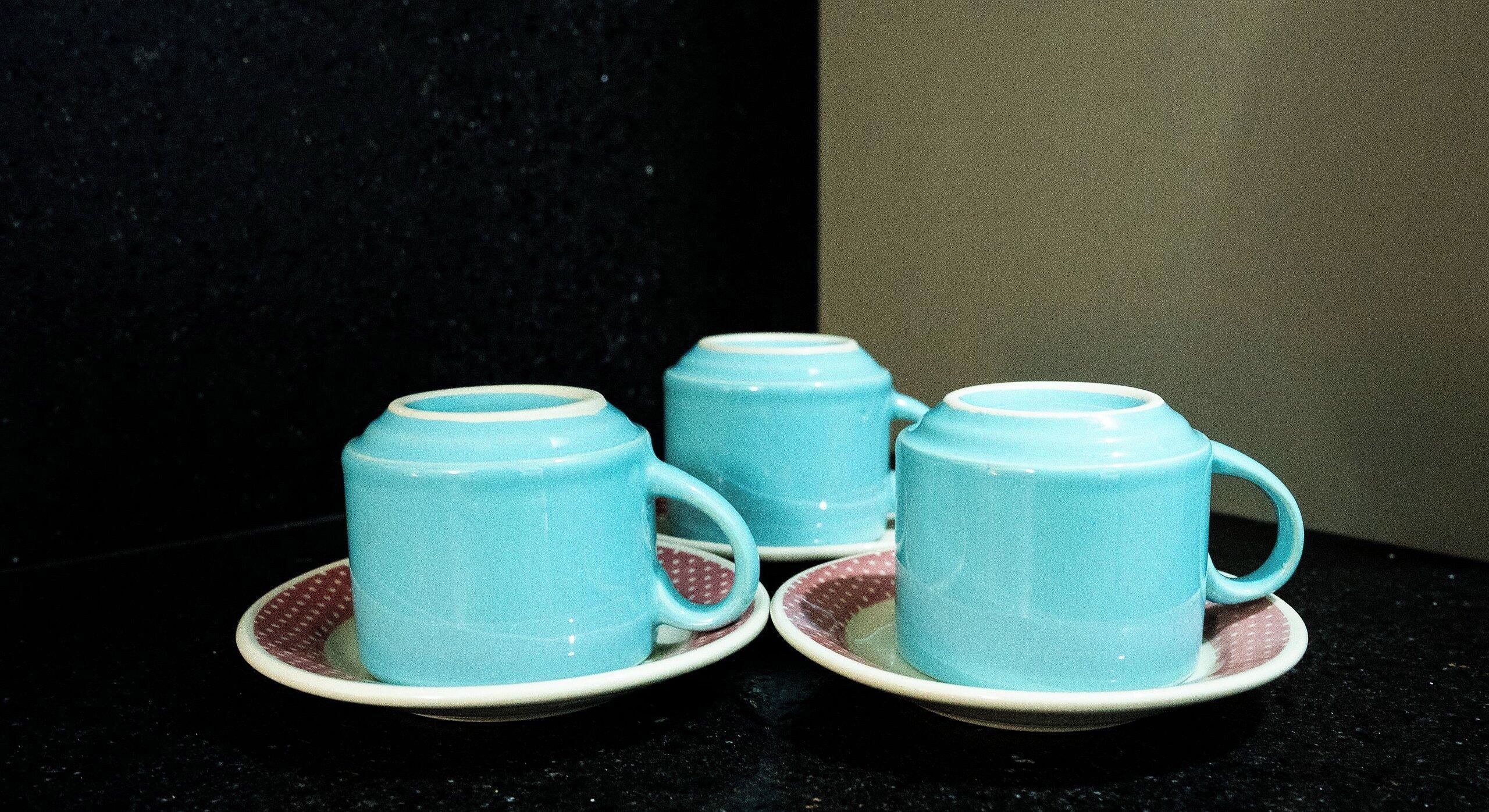 Tres tazas azules claras sobre platillos a juego, colocadas sobre una encimera oscura.