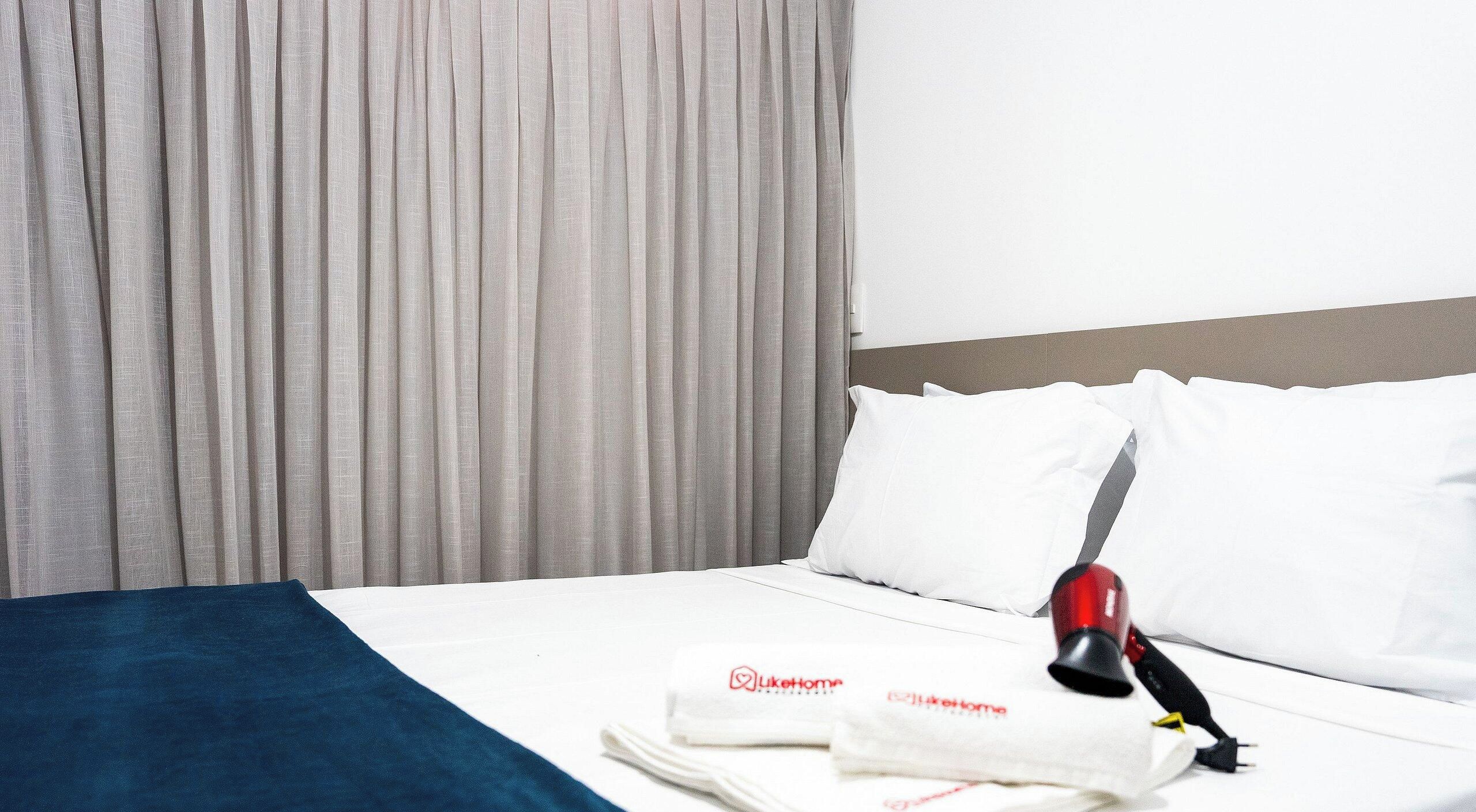 Een hotelkamer met een net opgemaakt bed, een rode en zwarte haardroger, en een handdoek met een logo.