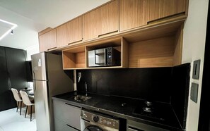 A modern kitchen with wooden cabinets, a built-in microwave, a stainless steel refrigerator, and a black countertop. - Move Tambaú (João Pessoa)