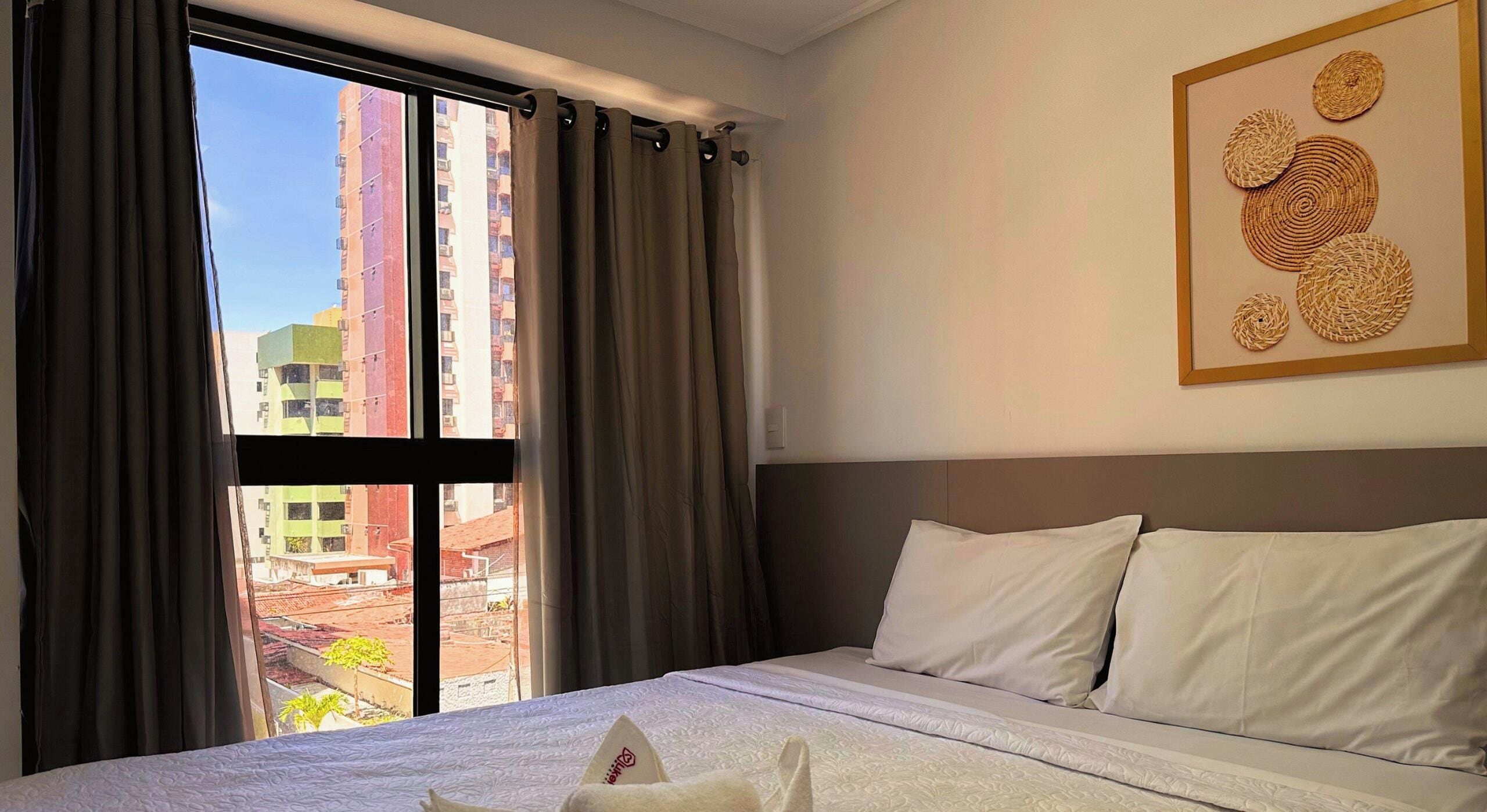 Habitación de hotel con cama, cortinas, ventana con vista a edificios y un cuadro en la pared.