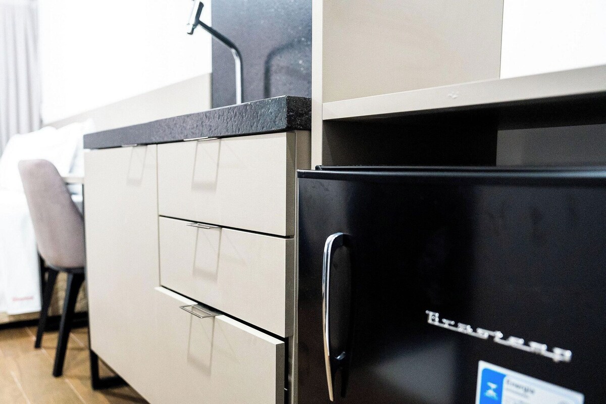 A compact kitchen with a refrigerator, a sink, and a chair.