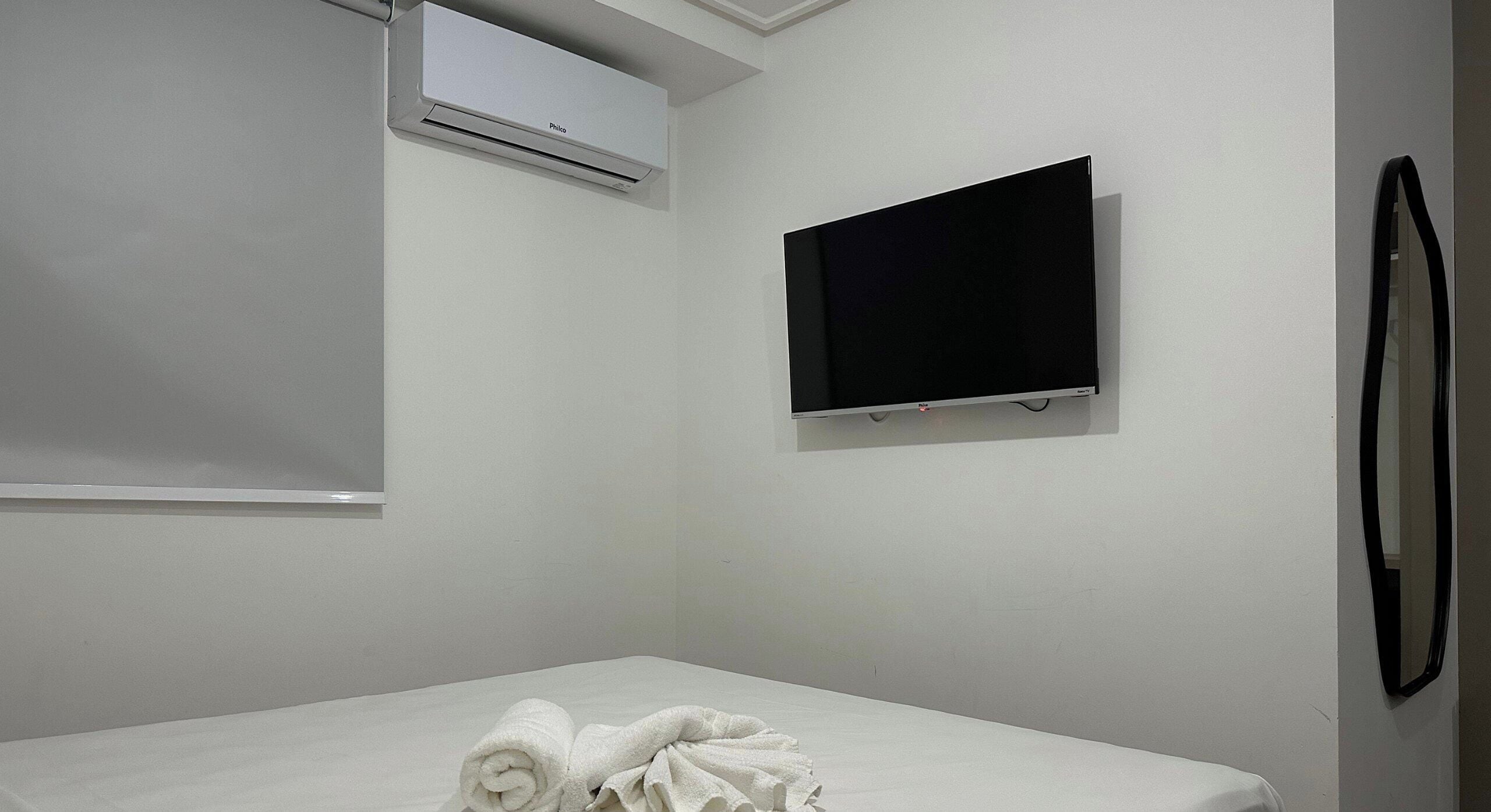 Ein Zimmer mit einem Bett, einem an der Wand befestigten Flachbildfernseher und einer Klimaanlage über dem Bett.