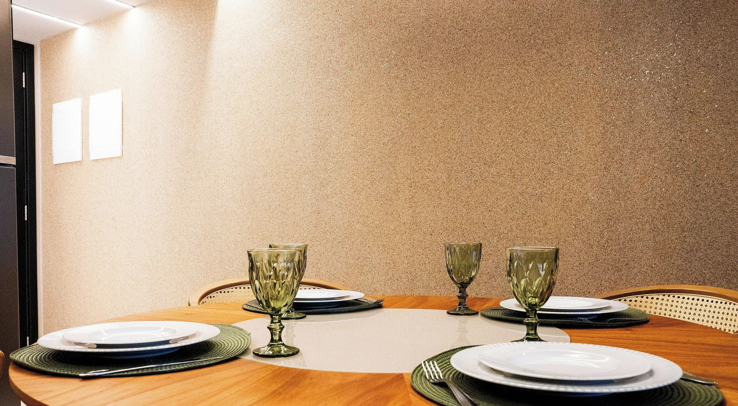 A dining table set for four with four wine glasses and plates, in a room with a textured wall and a door visible to the left.
