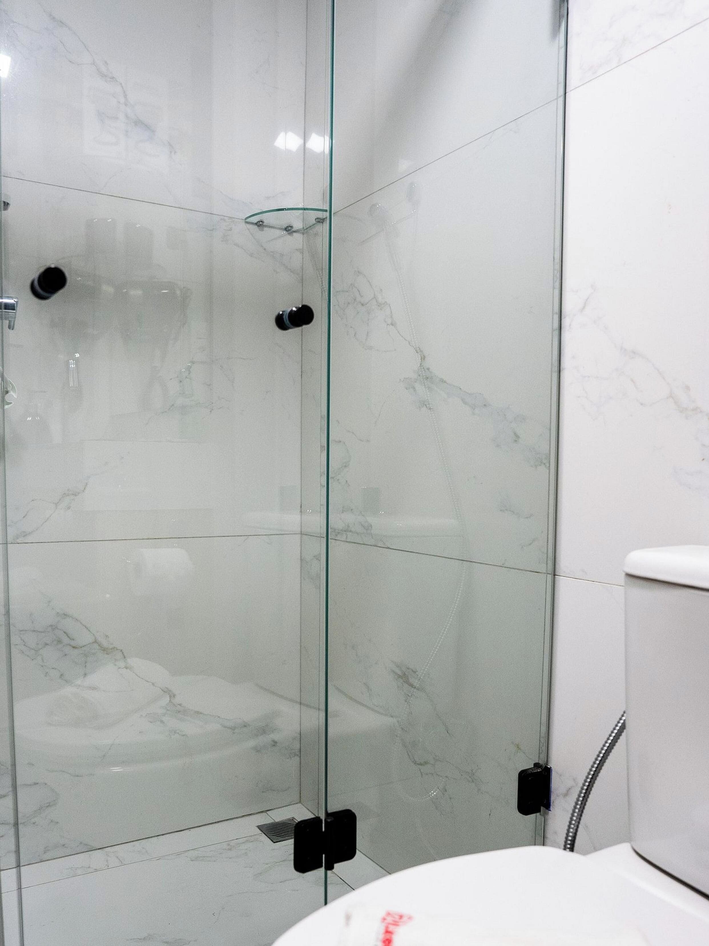 Um banheiro moderno com chuveiro em box de vidro, azulejos de mármore branco e vaso sanitário branco.