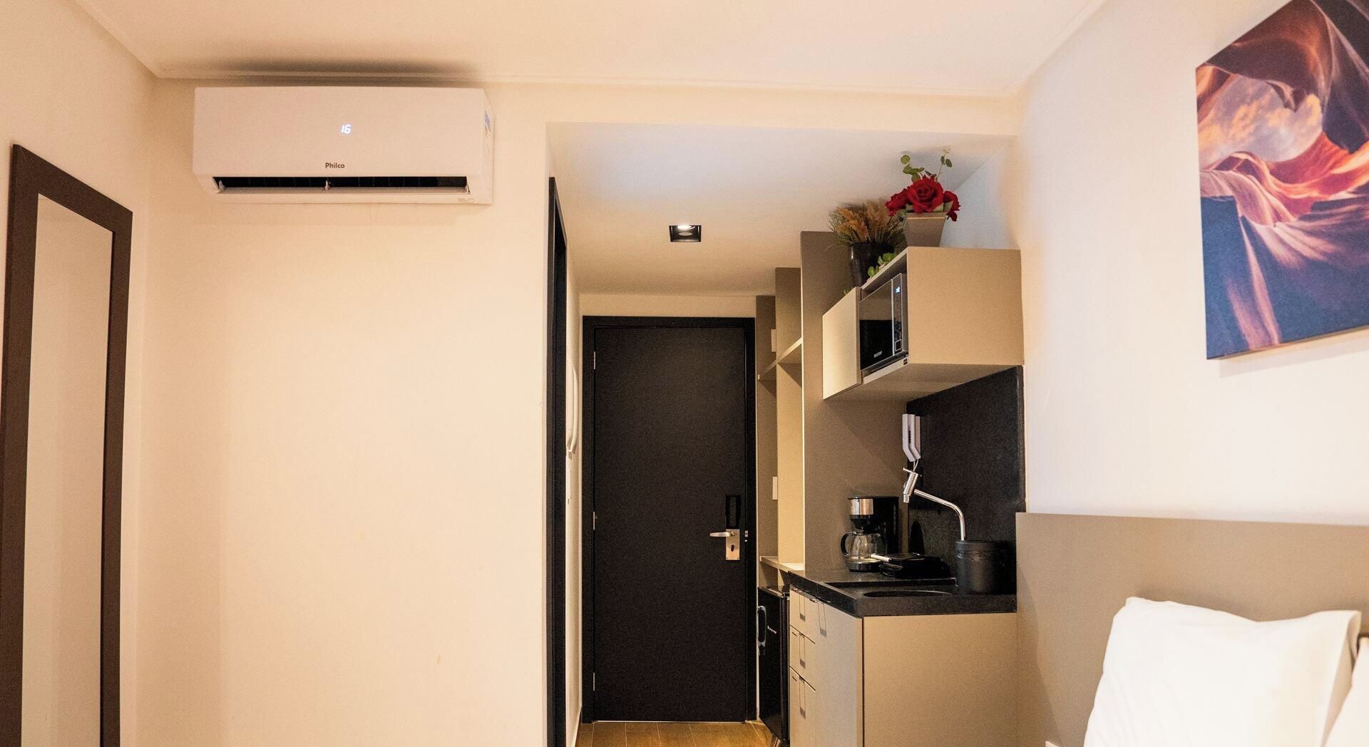 A compact hotel room with a kitchenette, a bed, and a painting on the wall.