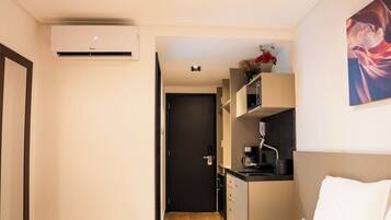 A compact hotel room with a kitchenette, a bed, and a painting on the wall.