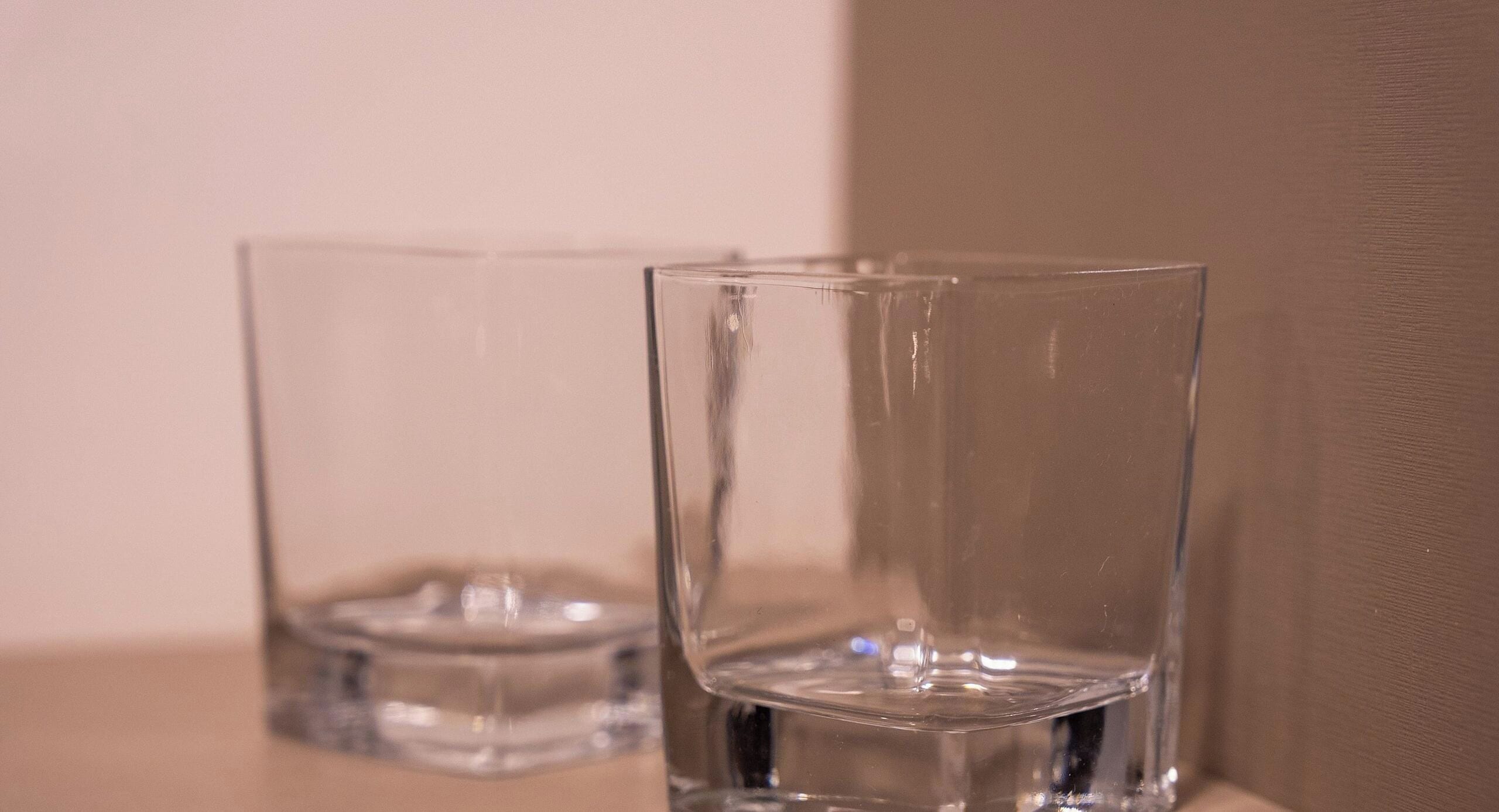 Two clear glass cups on a flat surface against a wall.