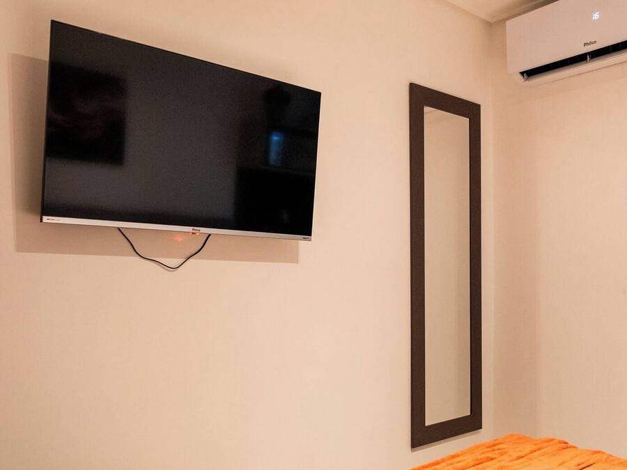 A television mounted on a wall with a black frame, an air conditioning unit above it, and a mirror to the right.
