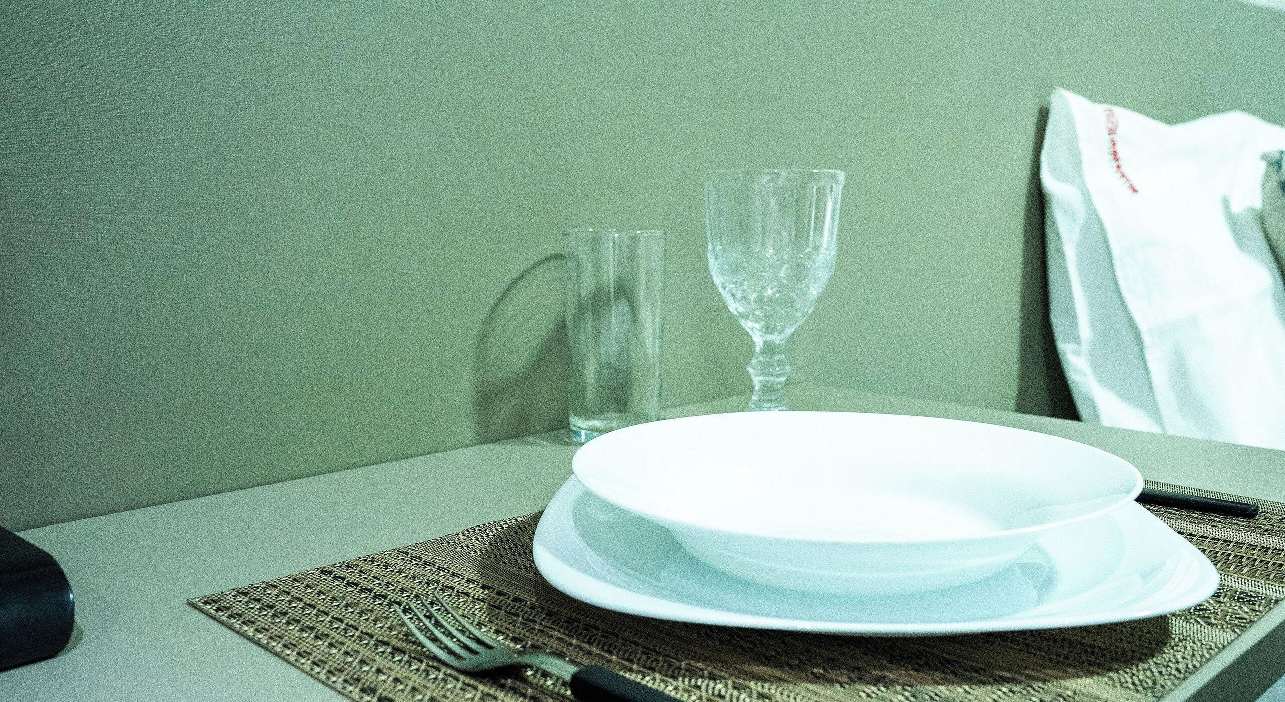 A table set with a white plate, a clear glass, and a fork on a woven placemat.