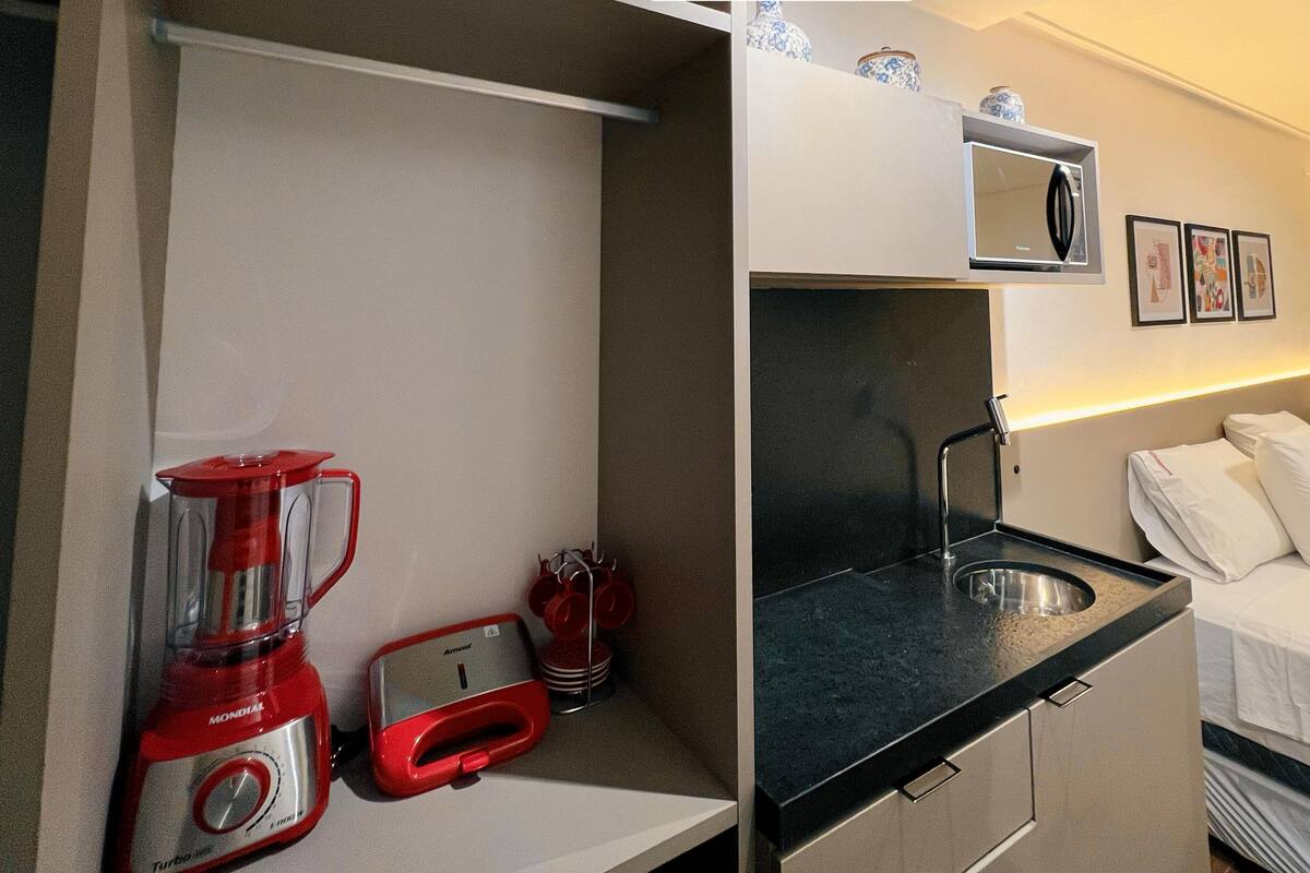 A compact hotel room with a kitchenette, a bed, and a small bathroom.