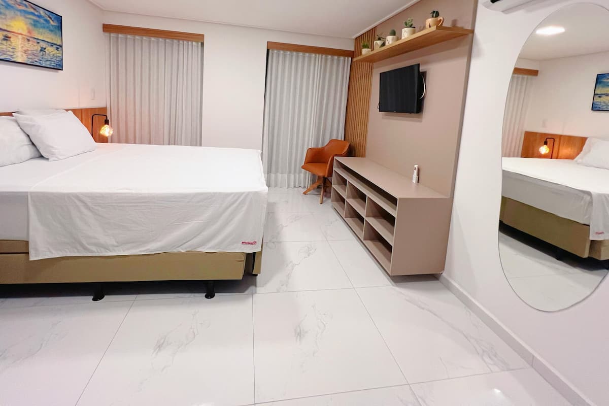 A hotel room with a large bed, a TV, a desk, and a chair.