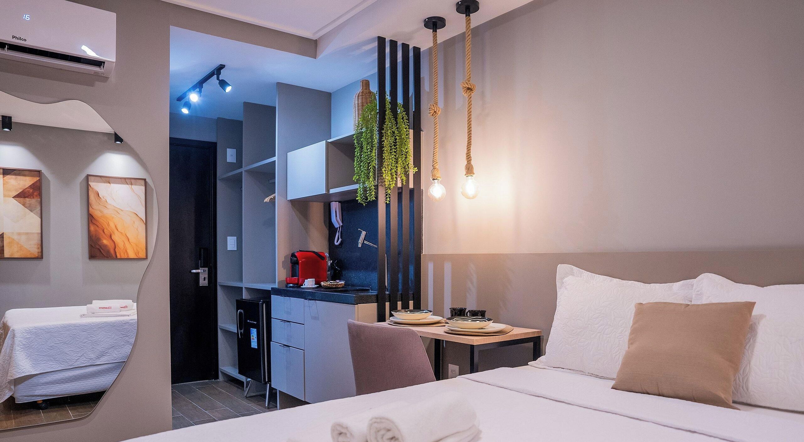 Een moderne hotelkamer met een bed, nachtkastje en een kleine kitchenette.