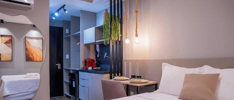 Een moderne hotelkamer met een bed, nachtkastje en een kleine kitchenette.