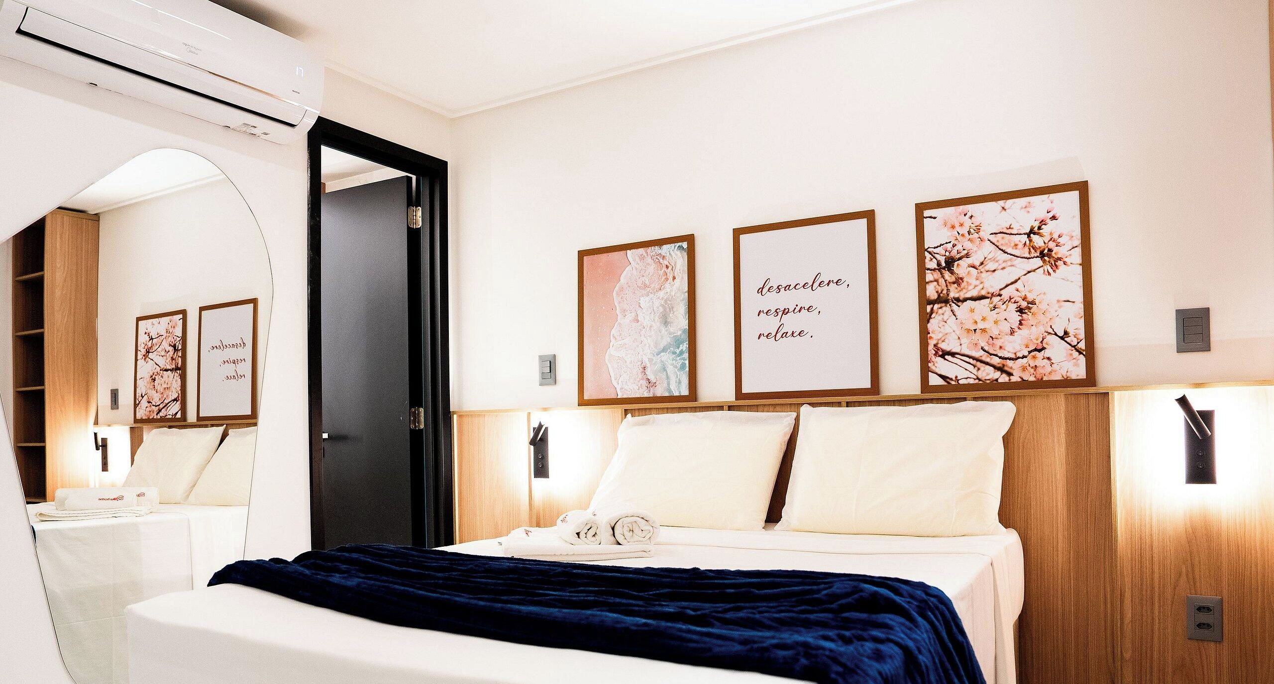 Hotellihuone, jossa on sänky, peili ja seinälle kiinnitetty taideteos.