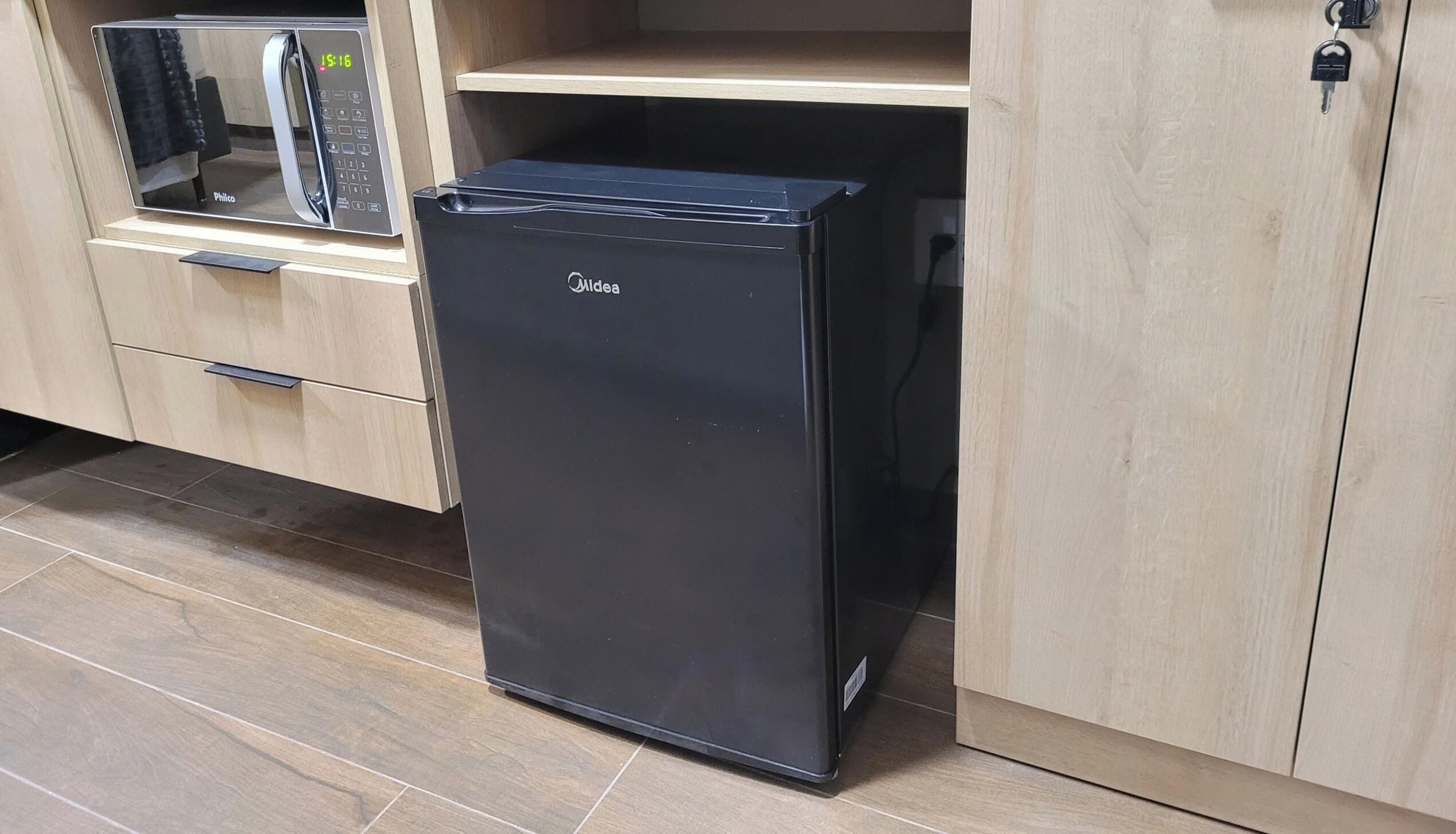 A compact black refrigerator with a digital display, situated in a kitchen with wooden cabinets and a tiled floor.
