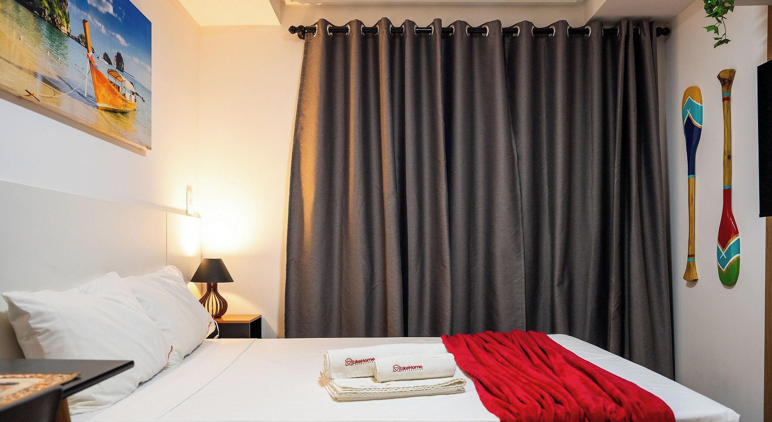 Hotellihuone, jossa on sänky, yöpöytä, lamppu, taulu ja verho.