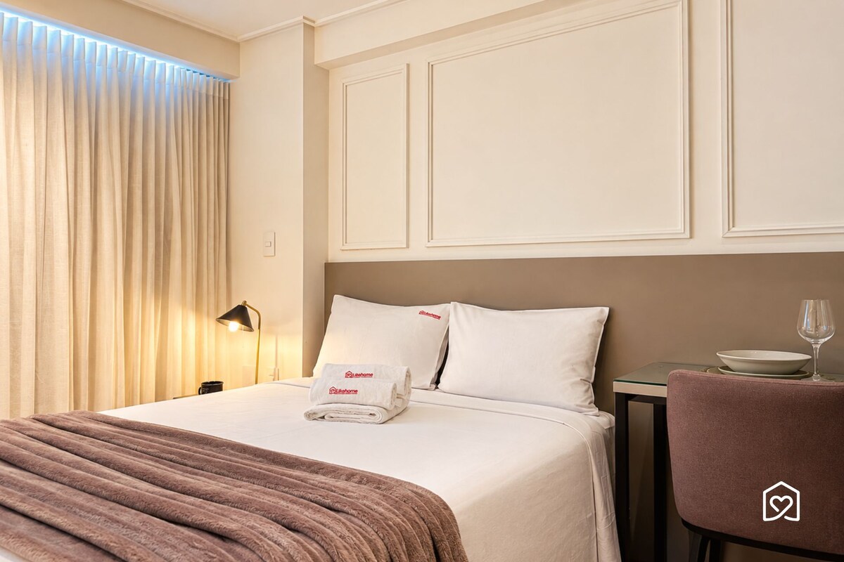 A hotel room with a bed, a nightstand, a lamp, a glass of water, and a chair.