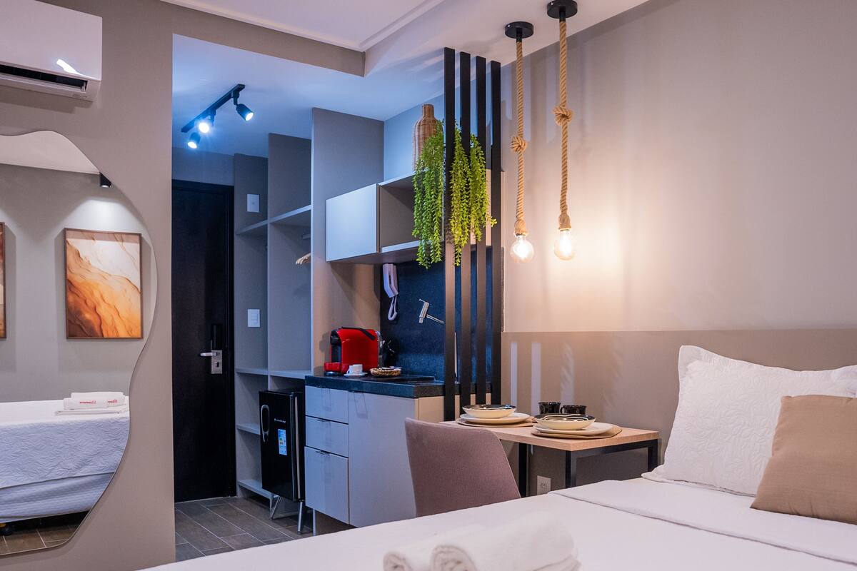 Ein modernes Hotelzimmer mit Bett, Schreibtisch, Küchenzeile und einem separaten Schlafbereich.