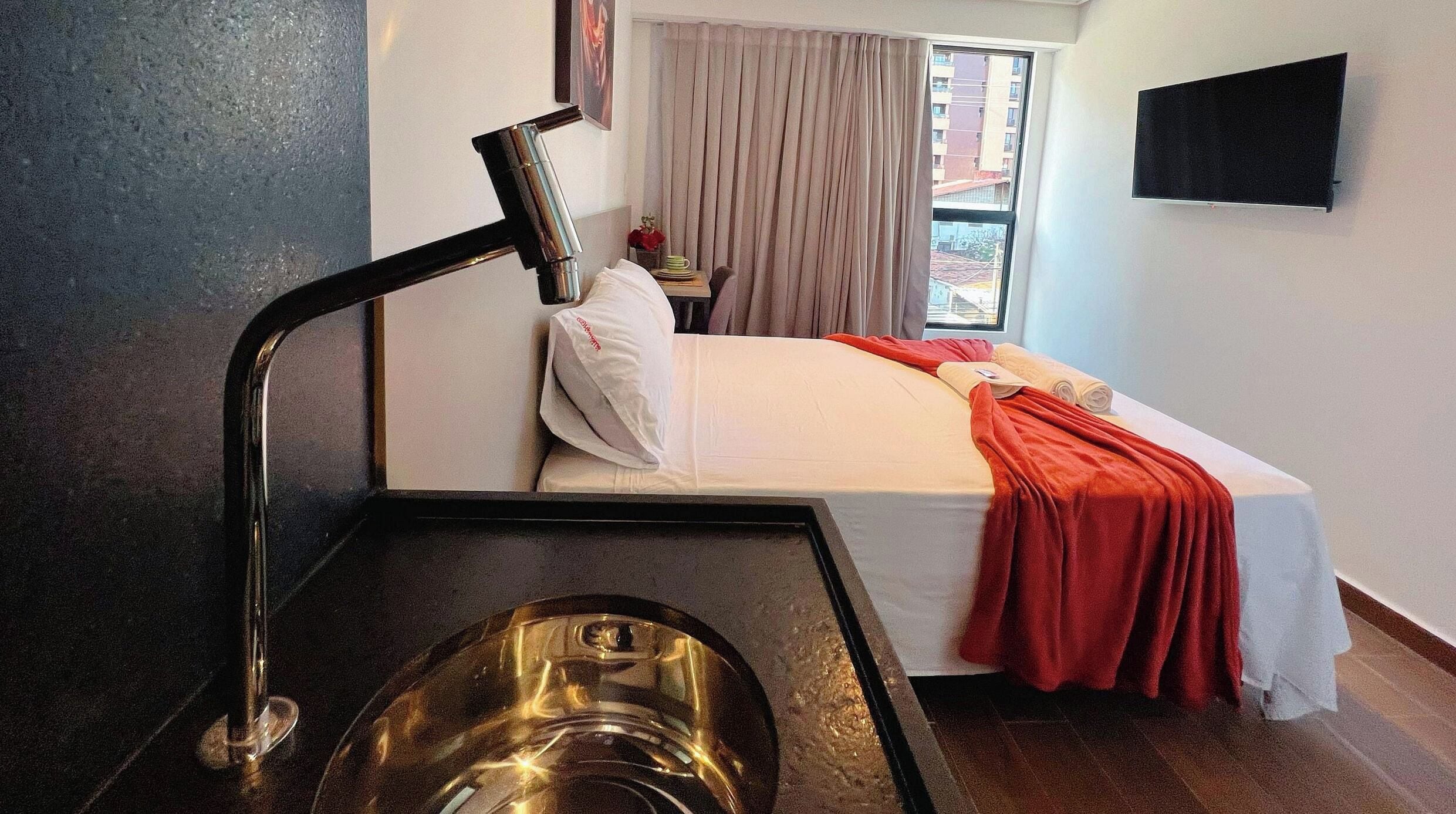 Een hotelkamer met een bed, een aan de muur bevestigde televisie en een wastafel.