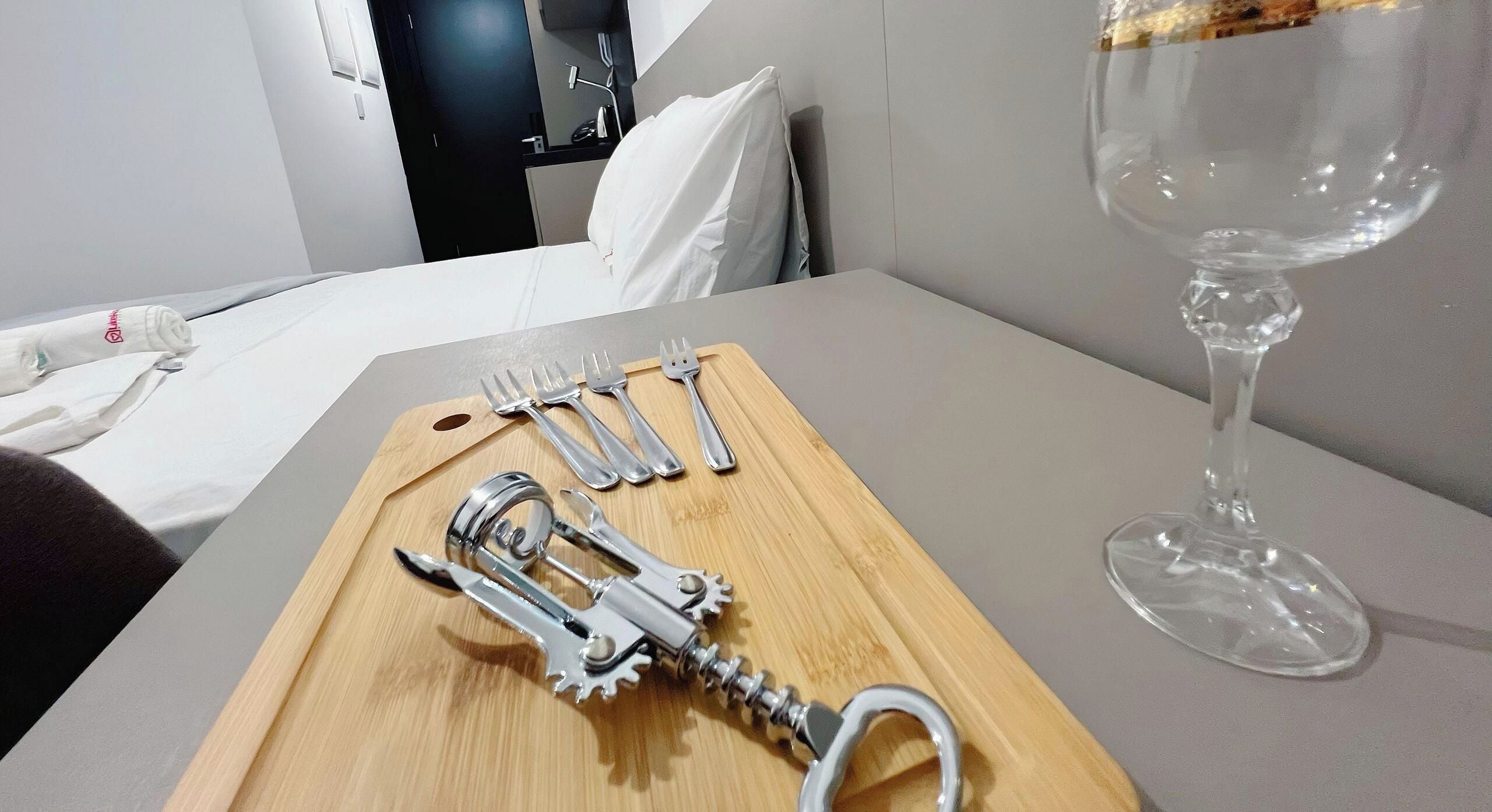 Una bandeja de madera con cubiertos y una copa de vino sobre una mesa en una habitación de hotel.