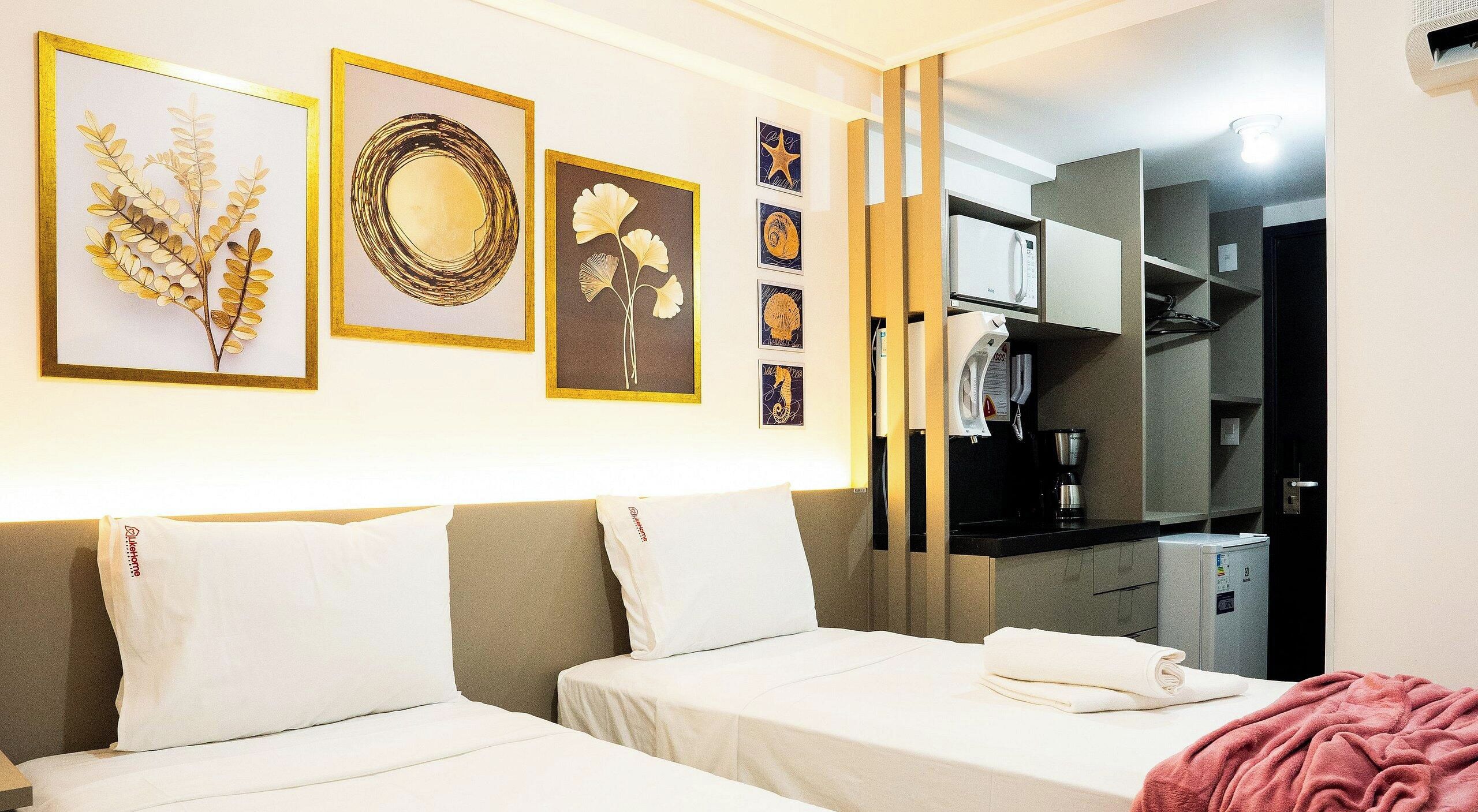 Habitación de hotel con dos camas, kitchenette y obras de arte colgadas en la pared.