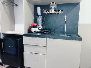 A kitchenette with a coffee maker, a blender, and a sink. There is a small black refrigerator and a white cabinet with drawers. - Move Tambaú (João Pessoa)