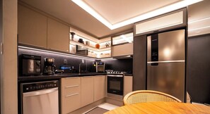 A modern kitchen with built-in appliances, a dishwasher, and a wooden dining table. - Move Tambaú (João Pessoa)