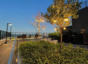 Un área de estar al aire libre con sillas y mesas, una barandilla y vistas al mar.
