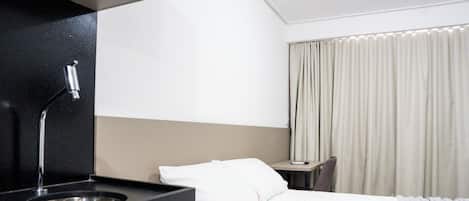 A hotel room with a bed, a desk, a chair, a sink, and a window with curtains.