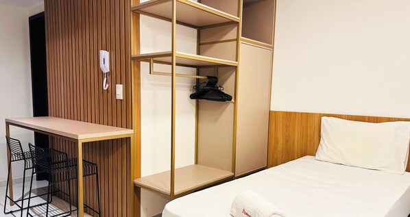 A hotel room with a bed, a desk with chairs, a wardrobe with multiple shelves, and a telephone. - Move Tambaú (João Pessoa)