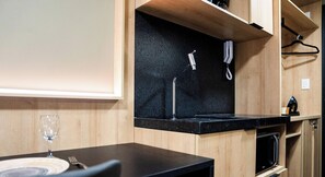 A compact kitchenette with a black countertop, a built-in oven, and a wine glass on a table. - Move Tambaú (João Pessoa)