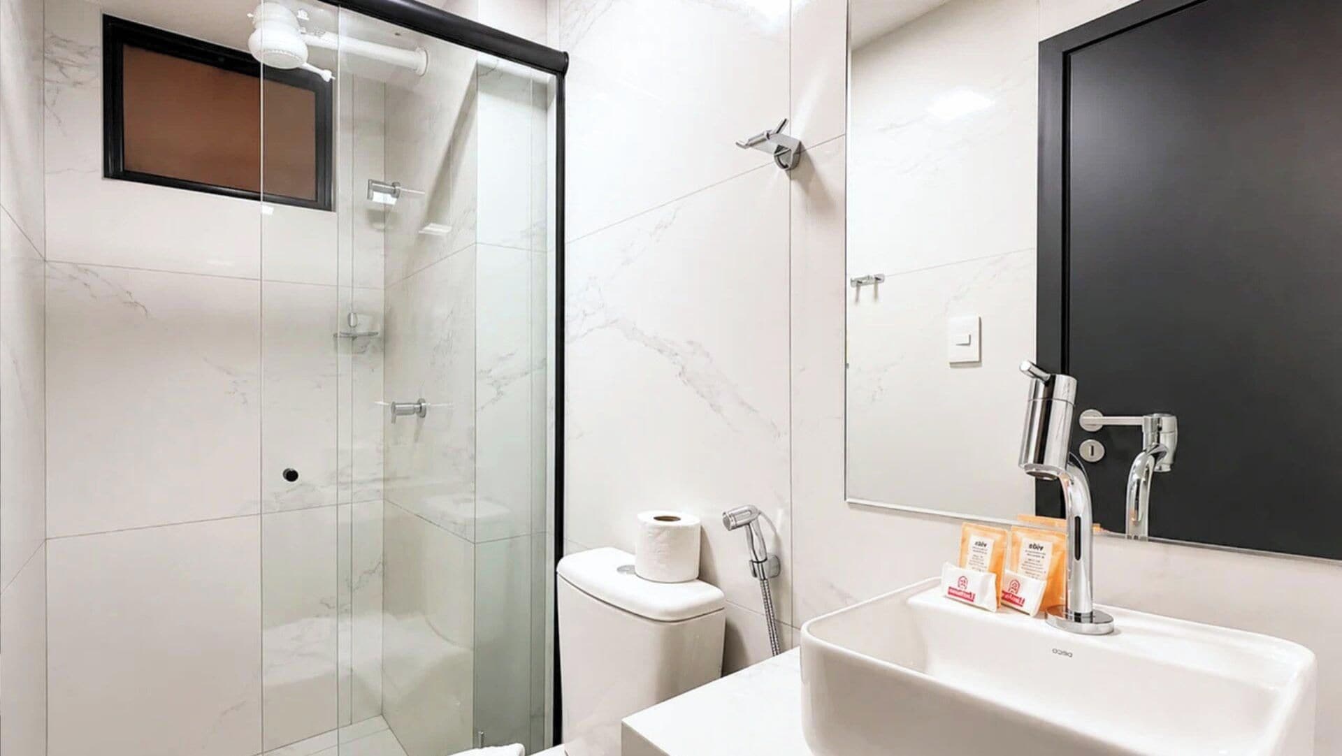 A modern bathroom with a glass-enclosed shower, a toilet, a sink with a mirror, and toiletries.