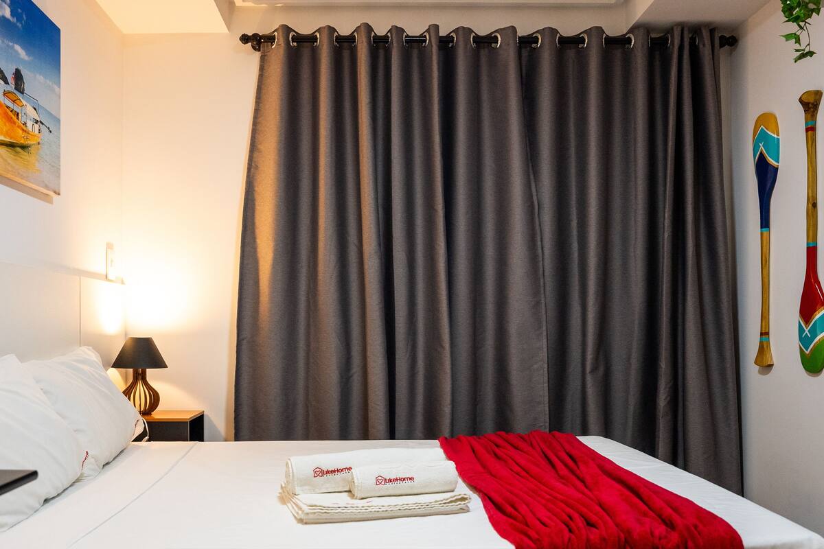A hotel room with a bed, a painting, a lamp, and a curtain.