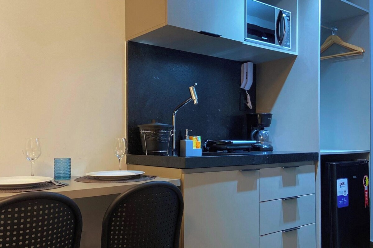 A compact kitchenette with a microwave, coffee maker, and a small refrigerator. There is a dining table with chairs and a wine glass.