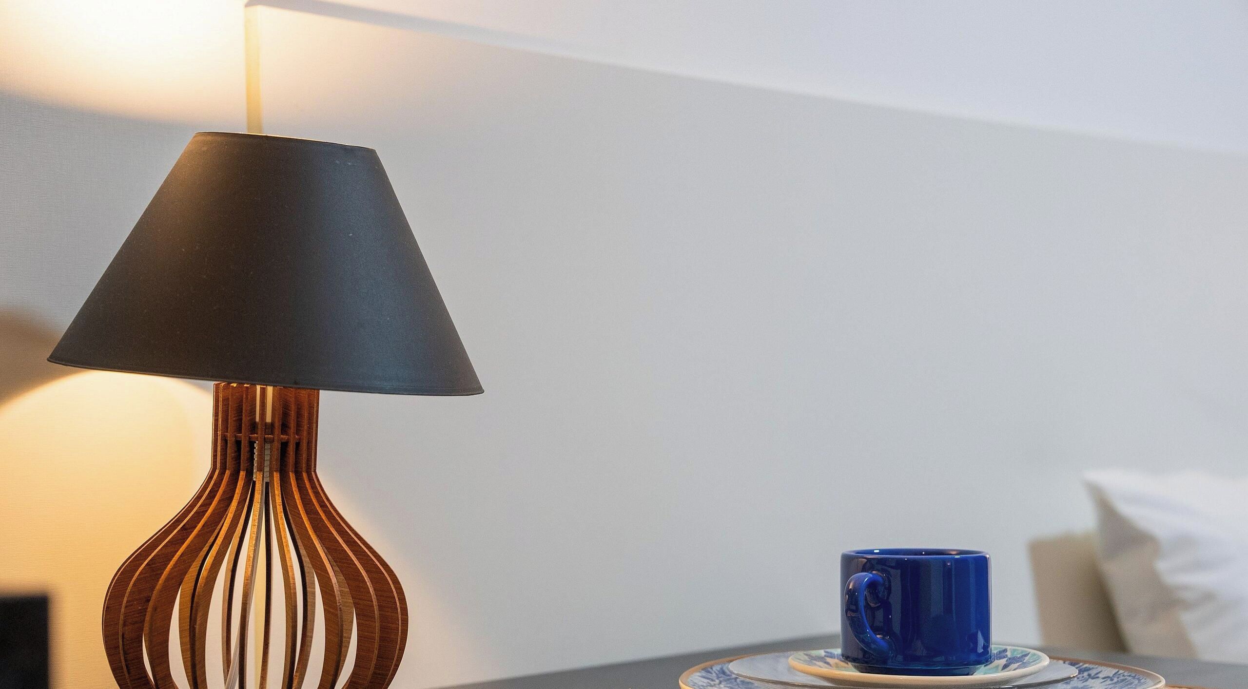 A lamp with a conical shade and a blue mug on a coaster.