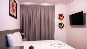 A hotel room with a bed, a TV, a painting, and a curtain.