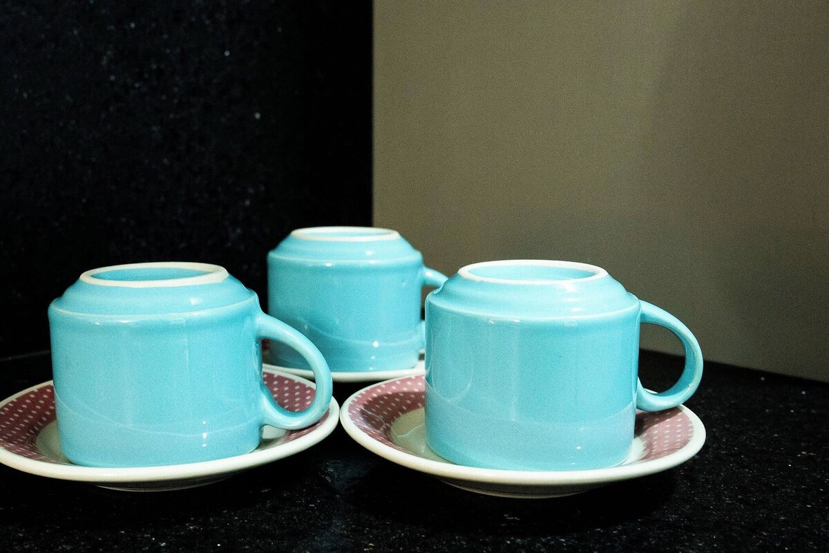 Three light blue ceramic cups with handles on matching saucers, placed on a dark countertop.