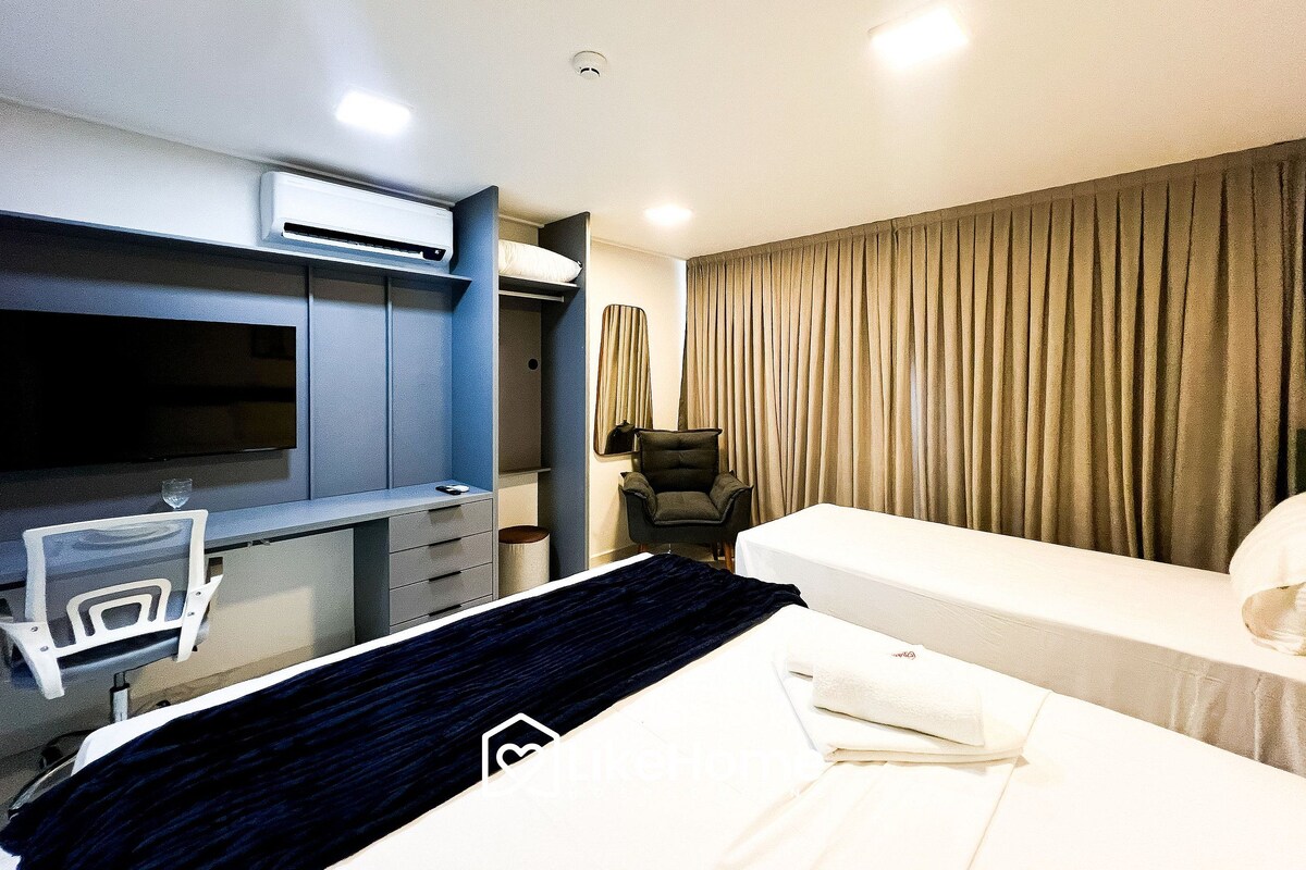 A hotel room with a bed, a desk with a chair, a television, and a large window with curtains.