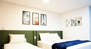 A hotel room with two beds, a green accent wall, and three framed pictures on the wall. - Move Tambaú (João Pessoa)