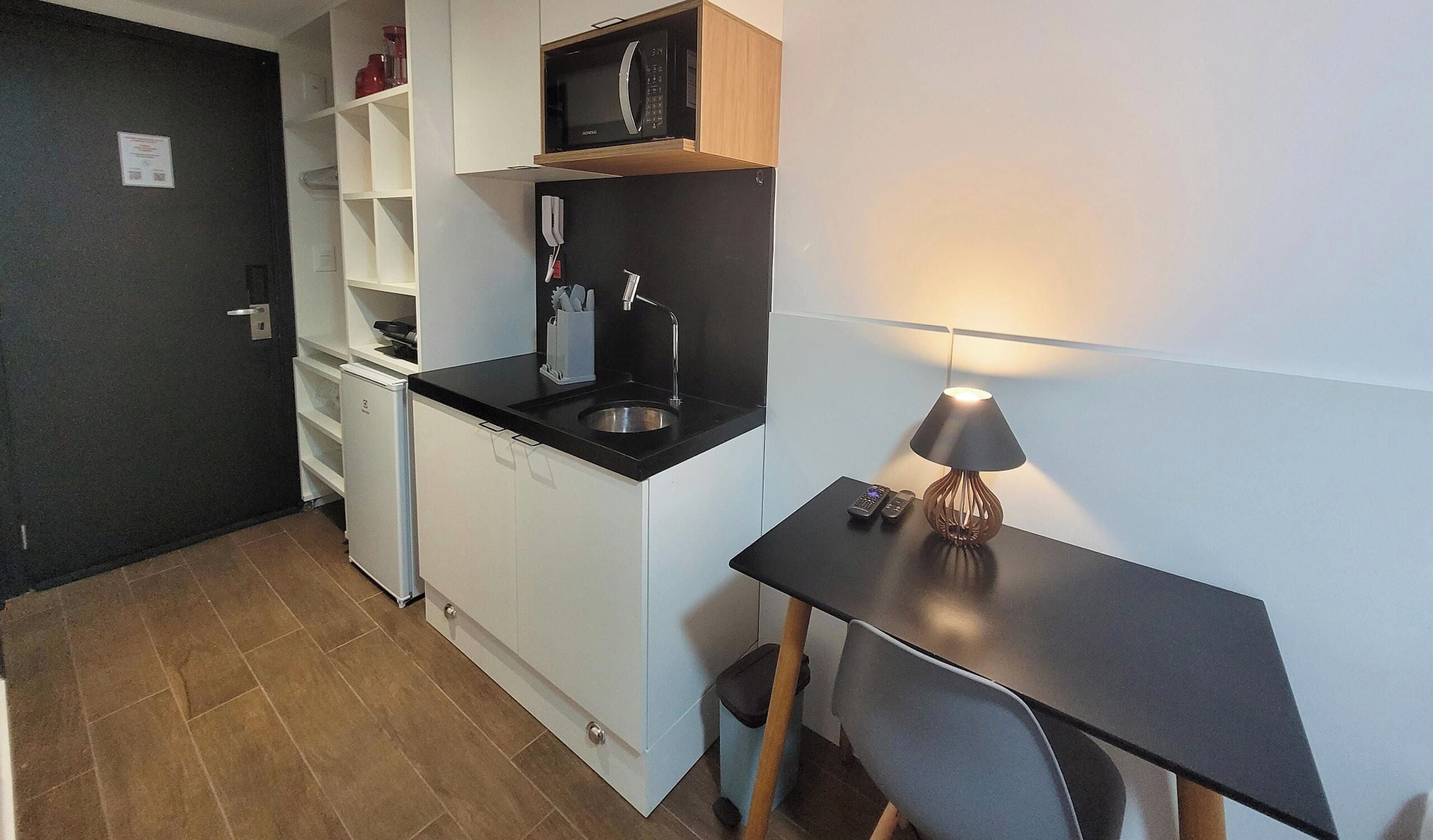 Una cucina compatta con microonde, macchina del caffè e un piccolo lavandino. C'è un'area pranzo con tavolo e lampada.