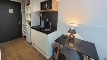 Una cucina compatta con microonde, macchina del caffè e un piccolo lavandino. C'è un'area pranzo con tavolo e lampada.
