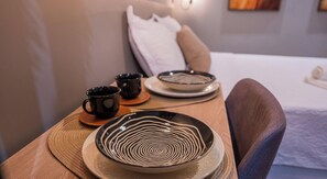 A table with a plate, two cups, and a bowl in a room with a bed and a pillow in the background. - Move Tambaú (João Pessoa)