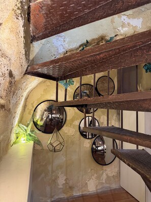 Un intérieur rustique avec des murs en briques apparentes, un escalier en métal et un grand miroir rond accroché au mur.