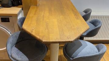 Une table en bois, quatre chaises bleues, une machine à café et un radiateur à l’arrière-plan.