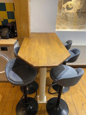 A wooden table with four blue chairs, a coffee machine, and a radiator in the background.