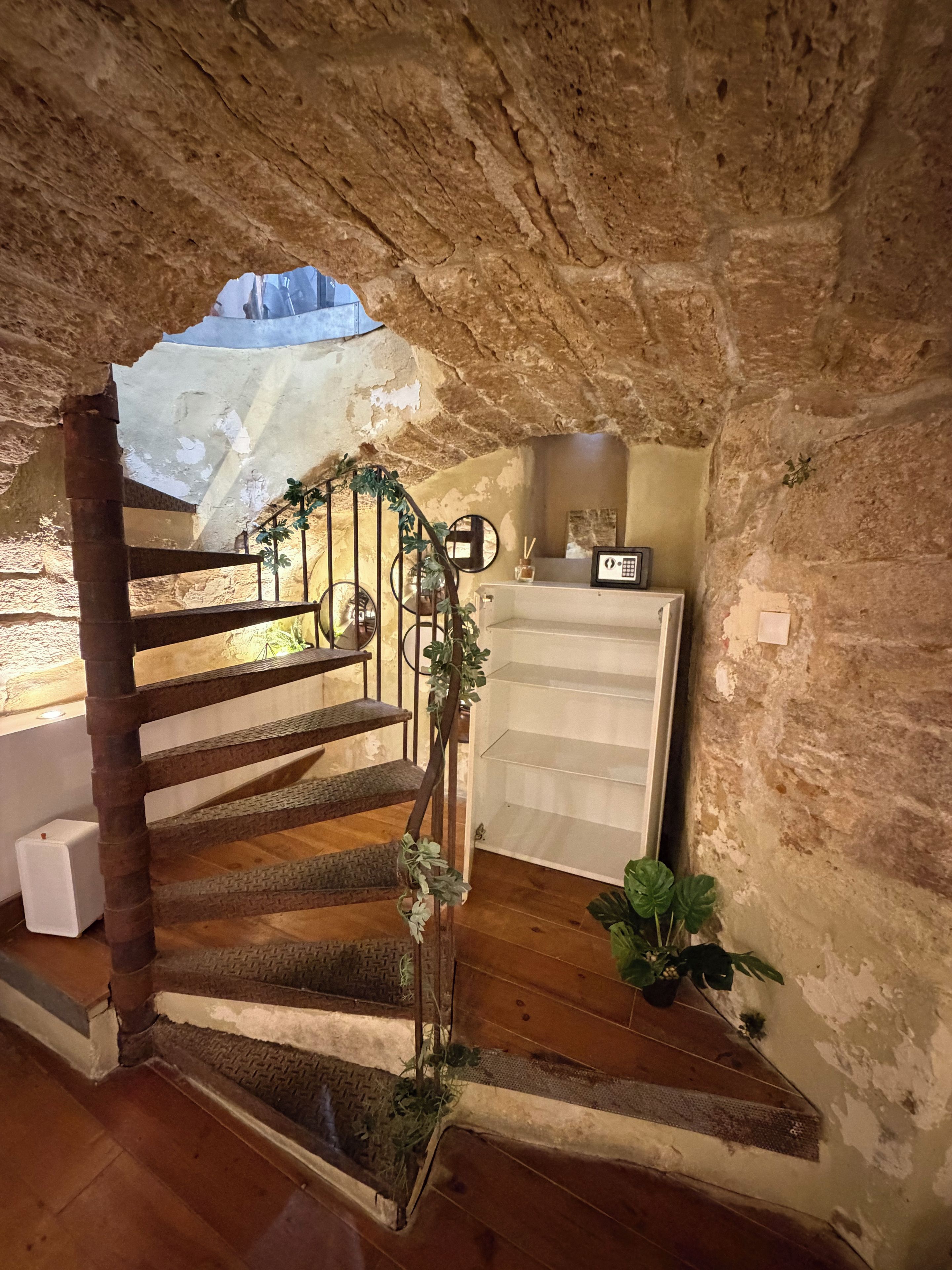 Eine Wendeltreppe im rustikalen Stil führt zu einem kleinen Raum mit Holzboden und einem weißen Regal.