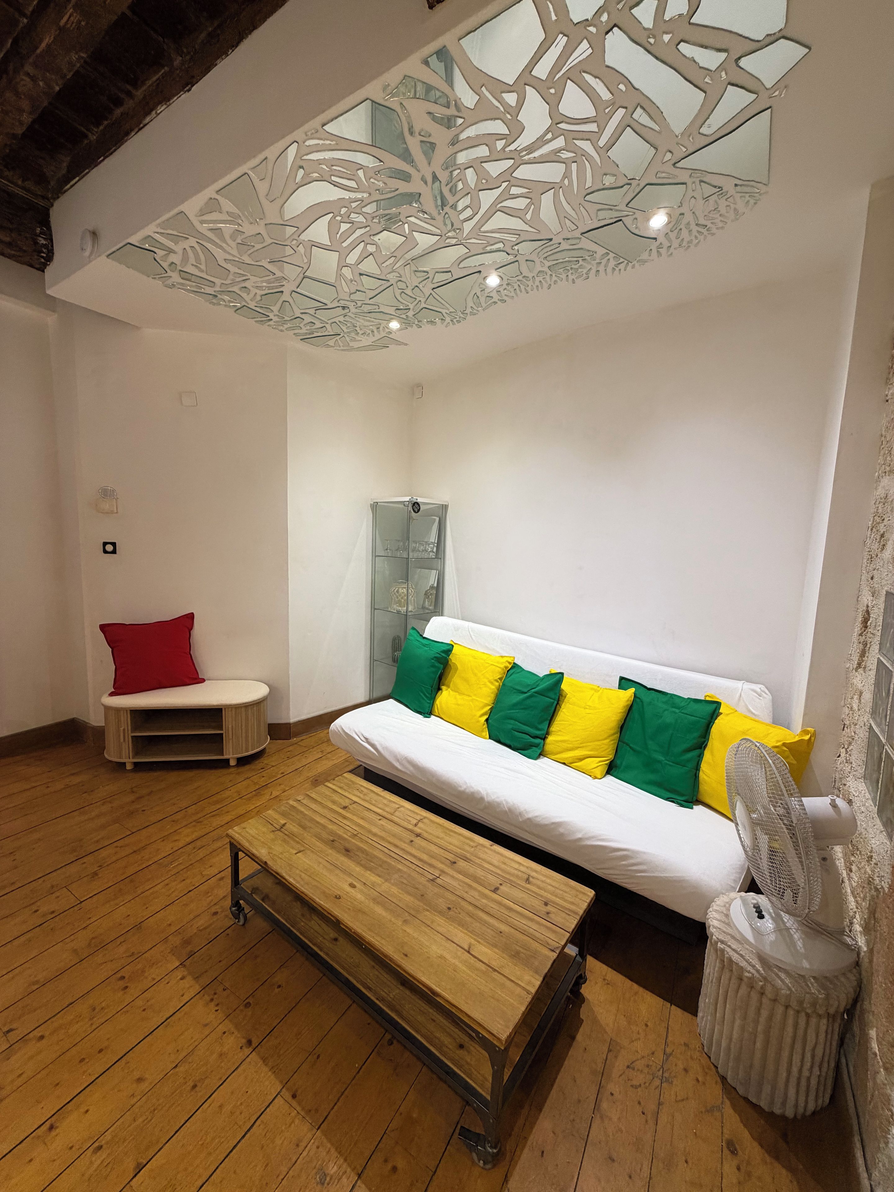 Une pièce avec un canapé blanc, un fauteuil rouge, une table en bois et un luminaire au plafond.