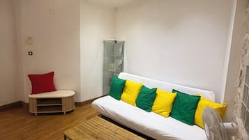 Une pièce avec un canapé blanc, un fauteuil rouge, une table en bois et un luminaire au plafond.